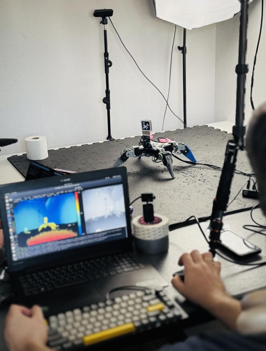 A small robot dog on a test mat, with a simulation on the laptop in front of it